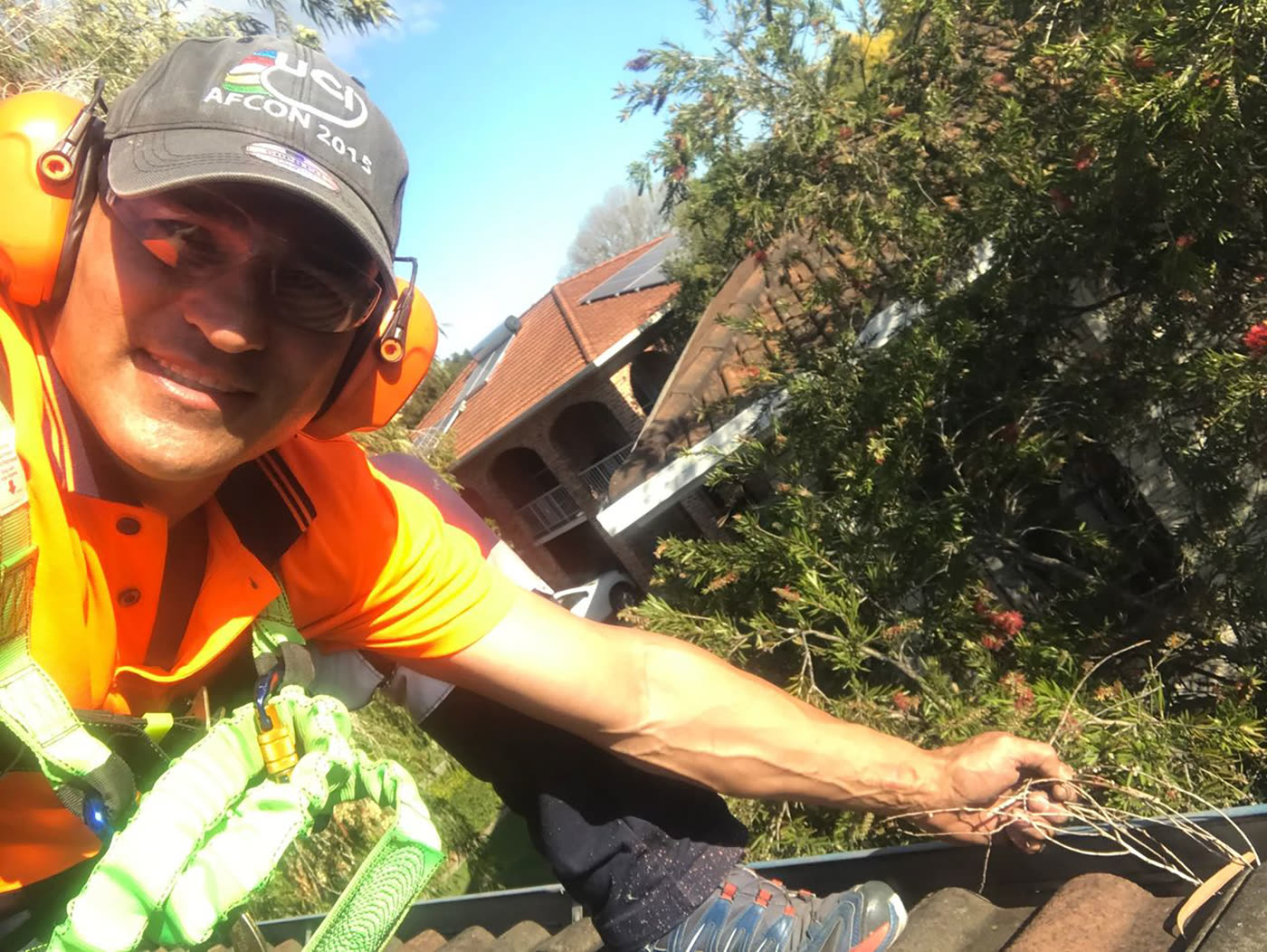 Rudi in full safety gear — hi-vis, ear protection and a harness — clearing a gutter on a tiled roof