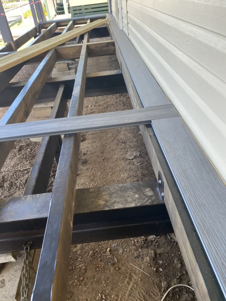 A deck stripped back to bare steel joists beside a weatherboard house