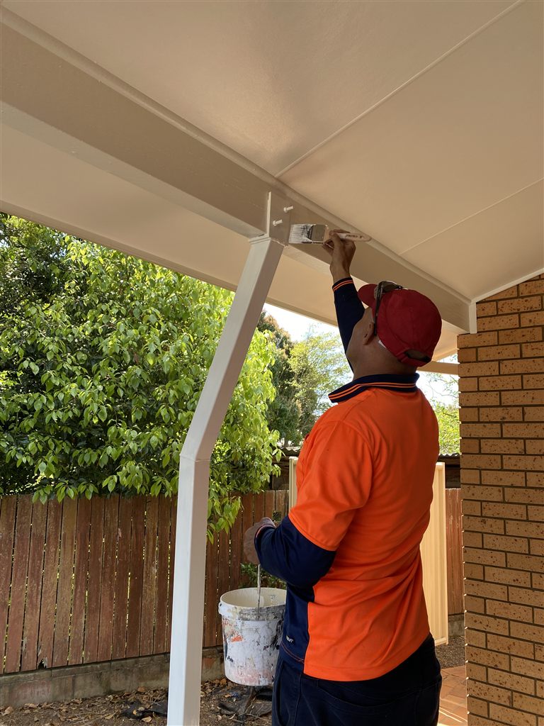 A tradesman in hi-vis painting the underside of an outdoor patio roof in cream